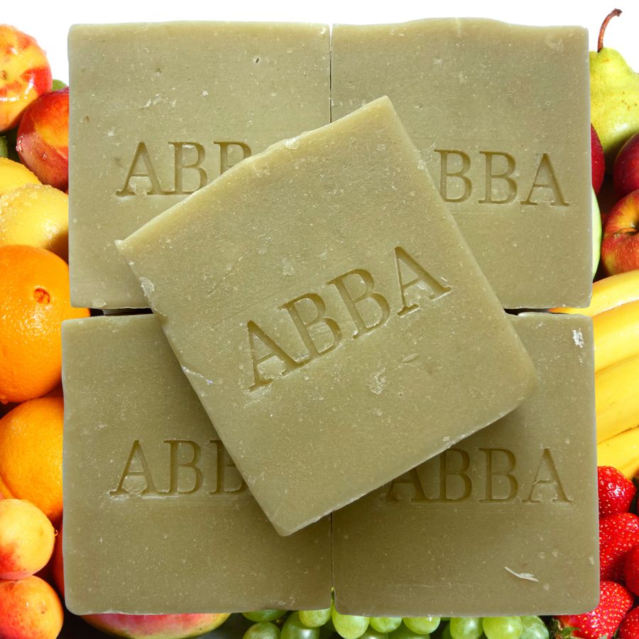Cuatro pastillas rectangulares de jabón artesanal de color verde oliva apiladas en forma de cuadrícula, con una barracolocada en diagonal en la parte superior. El jabón lleva grabado el nombre de la marca «ABBA».