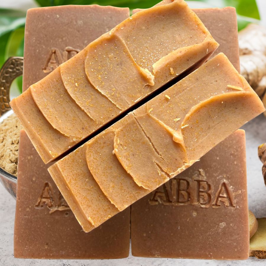 Cuatro barras de jabón artesanal de color marrón cálido, dispuestas de forma que se aprecie su textura en capas. Las pastillas llevan grabado el nombre de la marca «ABBA».