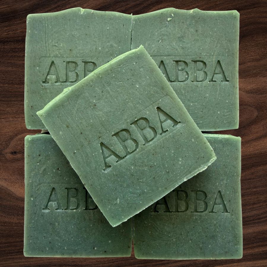 Cuatro barras rectangulares de jabón verde con la marca 'ABBA' grabada en la parte superior, dispuestas sobre una superficie de madera marrón oscuro.