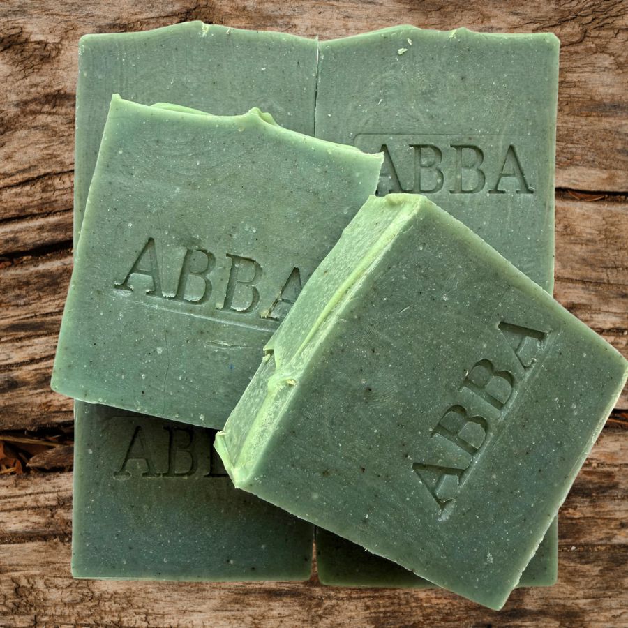 Cuatro barras de jabón rectangulares de color verde apiladas sobre una superficie de madera rústica, con la marca 'ABBAA' grabada en relieve en las pastillas superiores.